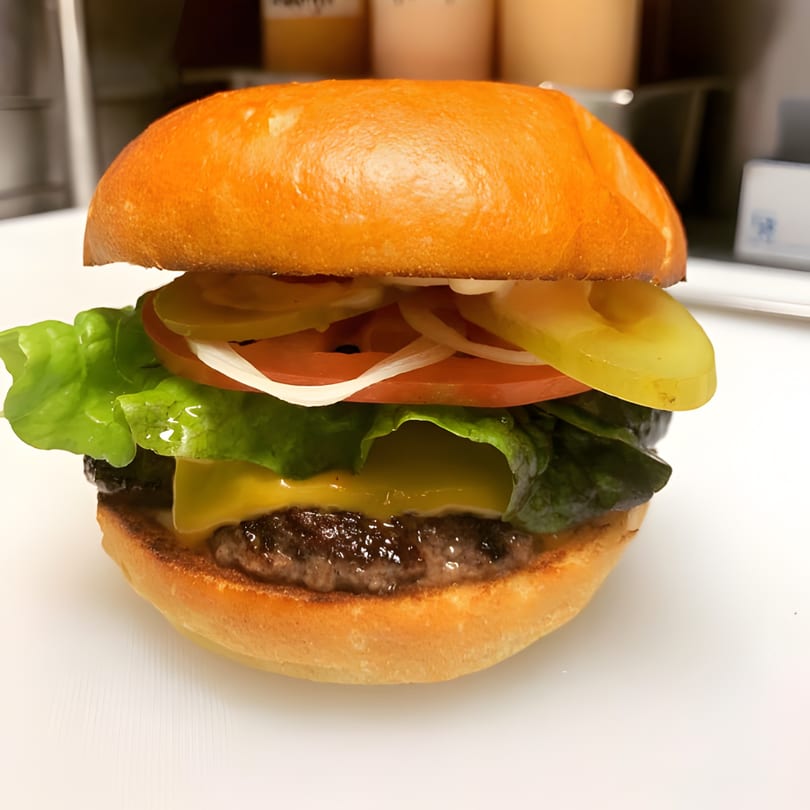 A Bushwick Burger Co. cheeseburger with lettuce, tomato, onion, and pickles on a brioche bun.
