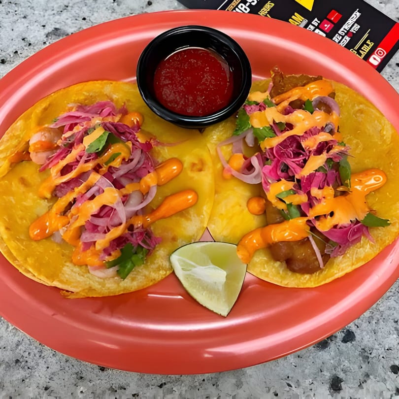Two vibrant tacos with red cabbage, sauce, and a lime wedge on a red plate.
