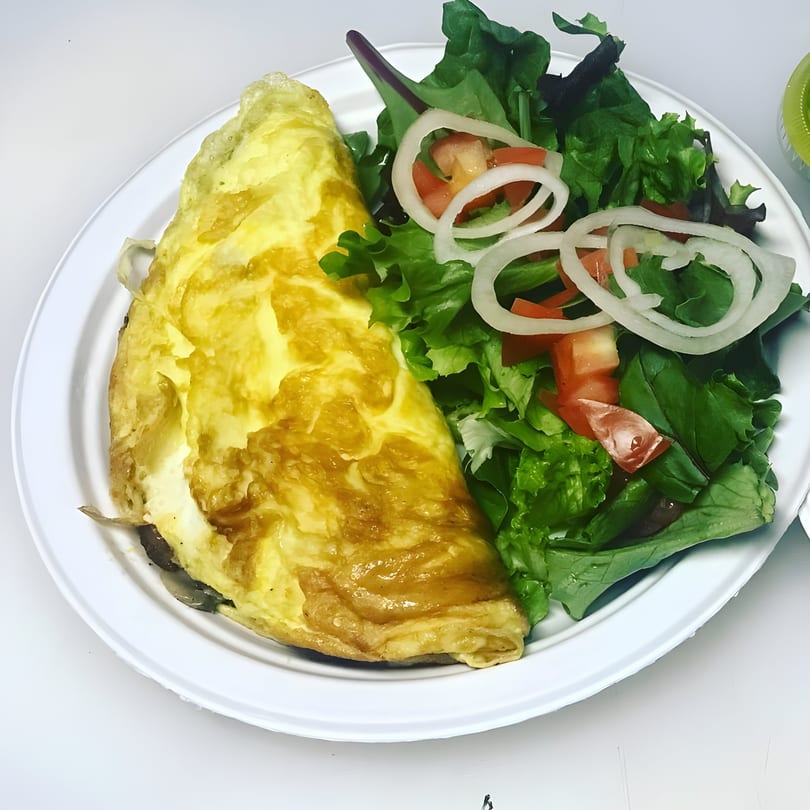A golden omelet and a fresh green salad with tomatoes and onion rings on a white plate.