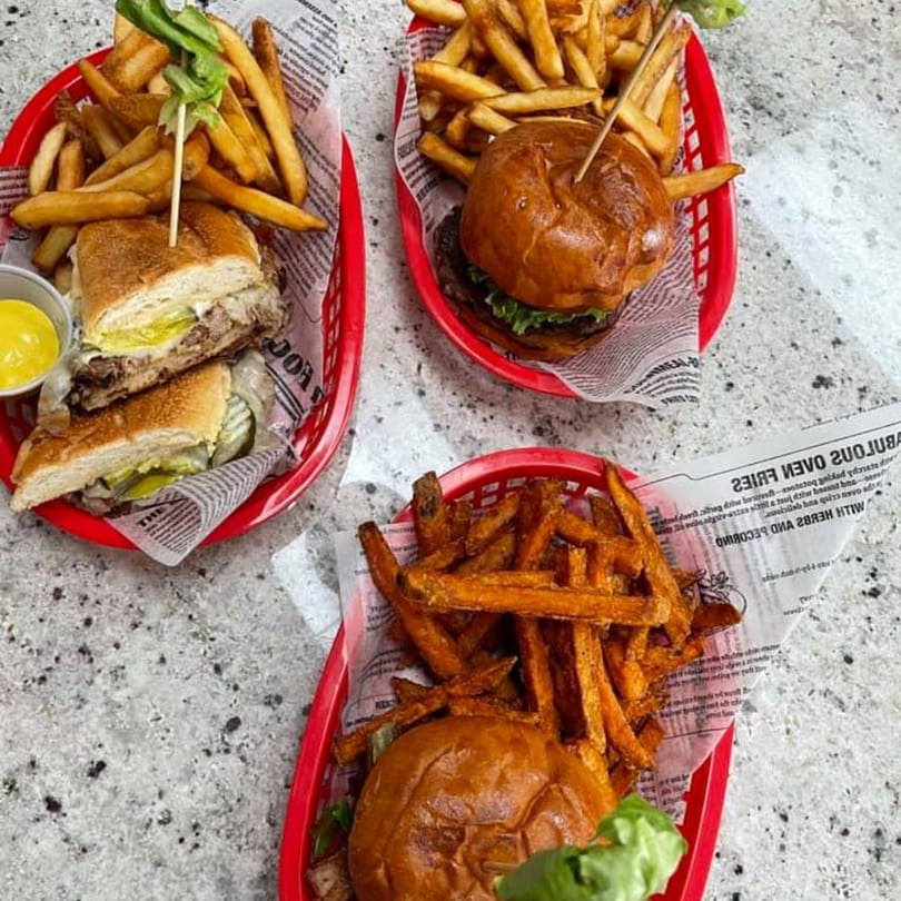 Three red baskets of Bushwick Burger Co. meals, including burgers, a Cuban sandwich, and fries.