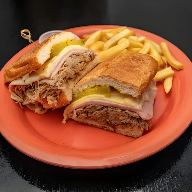 A Bushwick Burger Co. Cuban sandwich, cut in half, with fries on an orange plate.